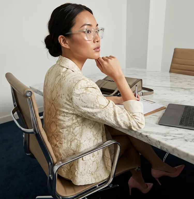 An executive seated at a marble table, thinking, with a laptop and notebook nearby.